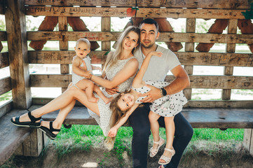 Portrait of a smiling mother and father sitting on a bench outside with their young daughters in...