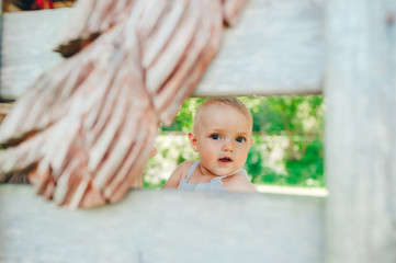 Closeup portrait of tricky face of baby girl hiding behind wooden fence.
