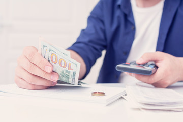 Man calculates his monthly expenses, man does not have enough money for all his debts, bills and calculator on the table, cropped image, closeup, toned