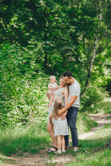 Fototapeta premium Parents and two cute little daughter in holds posing on the path in a sunny day in forest