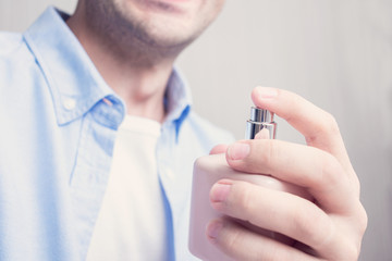 Young guy uses perfume, cropped image, closeup, toned