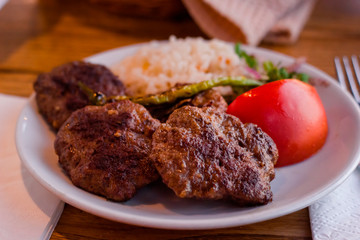 Cutlets and rice on a plate with tomato on table in evening sun light