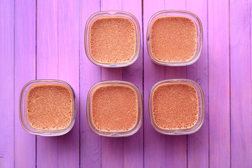Five portions of chocolate milk dessert are on a wooden table of purple. Breakfast dessert on a violet wooden background. Flat lay.