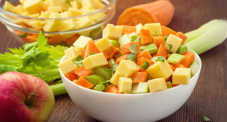 Vitamin salad of celery stalks, carrots, apples and cheese. Vegetable salad with cheese cut into cubes in a plate and a number of ingredients are.