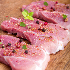 Raw pork steaks sprinkled with spices and herbs. Juicy raw steaks for a barbecue, close up.
