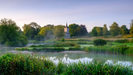 Misty dawn light on Stoke Charity village pond and St Michael's Church, Hampshire, UK