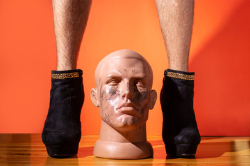 Man with on high heels with mannequin head man between hairy legs