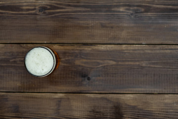 Glass of beer on dark wooden background. Top view. Empty space for text