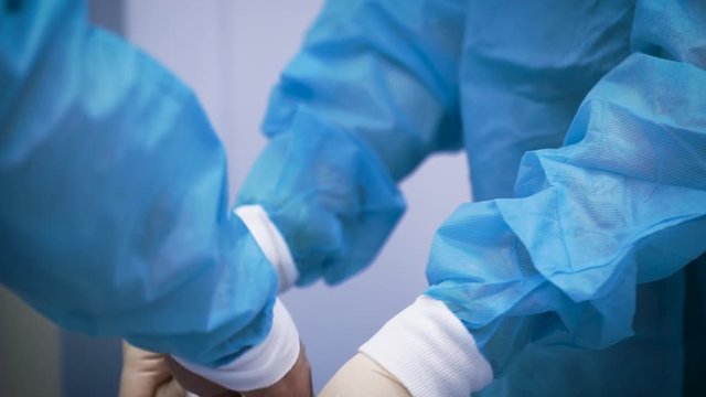 A nurse helps put a rubber glove on the doctor. Preparing for a complex operation, it is important to comply with the conditions of sterility, and other security protocols.