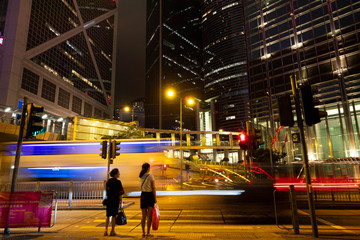 近未来都市的な高層ビル群を通過する光る乗り物と通行人たち