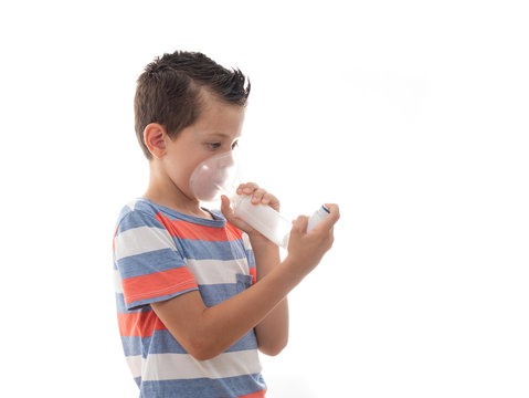 portrait of a 6 year old young boy using an inhaler mask for treating an asthma attack isolated on white background