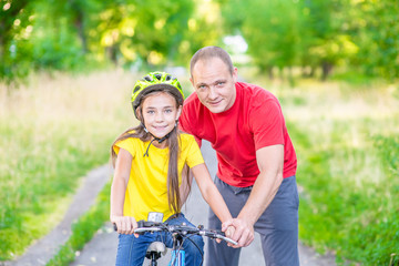 Active family leisure. Father teaches his daughter to ride a bicycle in the summer park