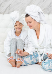 Mother and daughter are doing pedicures at home. Mom and child girl are in bathrobes and with towels on their heads