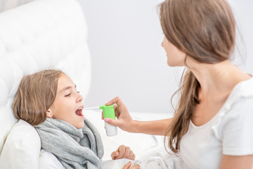 Obraz na płótnie Canvas Woman using medical spray for young girl at home