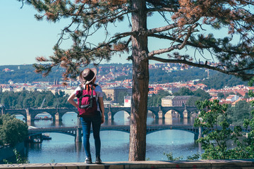 Young female tourist in a cowboy hat with sunglasses and a backpack, enjoying great view on the old town of Prague. Praha, Travel tour to Europe.