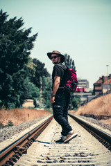A man with a backpack goes ahead on the railway track during the summer season. Long way concept, forward. achieve your goal, the beginning of the path. cowboy hat and glasses, vertical photo