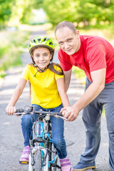 Obraz premium Happy family. Father teaches his daughter to ride a bicycle in the summer park