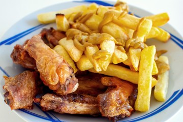 Grilled chicken wings with crispy french fries and mustard on them inside a white plate.