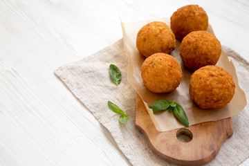 Homemade fried Arancini with basil on a rustic wooden board, side view. Italian rice balls. Copy space.
