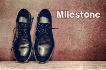 Milestone on brown board and work shoes on wooden floor