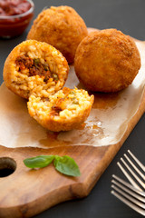 Homemade fried Arancini with basil and Marinara sauce on a black surface, side view. Italian rice balls. Close-up.