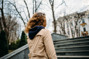 A young woman in a beige coat climbs the stairs