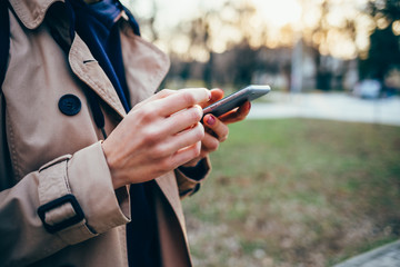 Woman in a beige coat holds a mobile phone