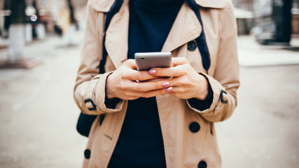 Young woman in a beige coat holds a mobile phone
