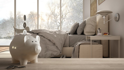 Wooden table top or shelf with white piggy bank with coins, modern panoramic bedroom with window and bed, expensive home interior design, renovation restructuring concept architecture