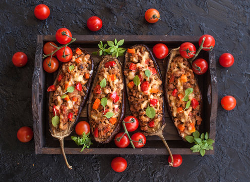 Stuffed with minced meat and vegetables eggplant-a delicious healthy lunch on a wooden tray on a black slate background. Snack. Top view