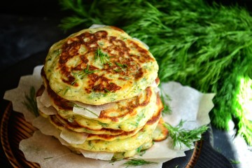 Appetizing pancakes on a wooden board. A photo of food in low key. Pancakes with parsley and chives. Ukrainian and Russian cuisine. Food on a black background. Pancake week.