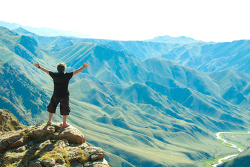A man with outstretched arms standing in the mountains.