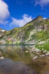 Fototapeta na wymiar Flock of small fish, ripple in the clean, transparent water of famous Kidney lake, one of seven Rila lakes, epic, sunlit rocky summits and a blue sky with white clouds