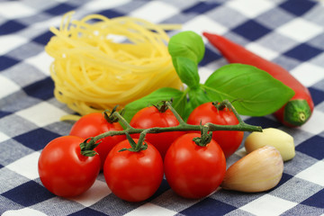 Pasta ingredients: uncooked tagliatelle, cherry tomatoes on stem, fresh basil leaves and red chili
