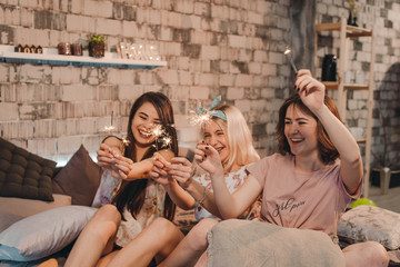 Awesome ladies in pajamas enjoying the time together in the bedroom playing with a sparkling fireworks, at sleepover night party