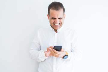 Middle age man using smartphone over white wall with a happy face standing and smiling with a confident smile showing teeth