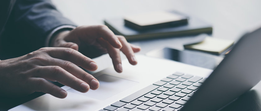 Businessman is using laptop and analysing the financial information at his office. Close up of male hands typing on computer keyboard