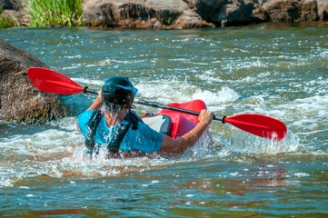 Playboating. A man sitting in a kayak with oars in his hands performs exercises on the water. Kayaking freestyle on whitewater. Eskimo roll.