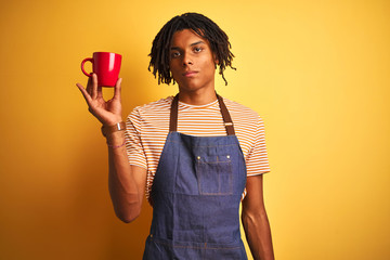 Afro barista man with dreadlocks drinking cup of coffee over isolated yellow background with a confident expression on smart face thinking serious