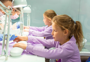 Two little twin girls in a nail salon receiving a manicure. Selective focus