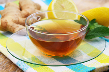Tea in transparent cup with lemon, mint and ginger in the background
