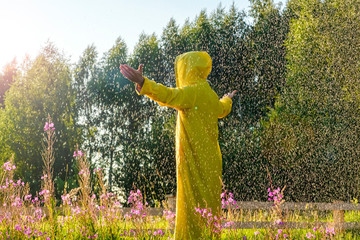 A man in a yellow raincoat stands in the rain and looks forward, raising his hands to the sky. hiking concept