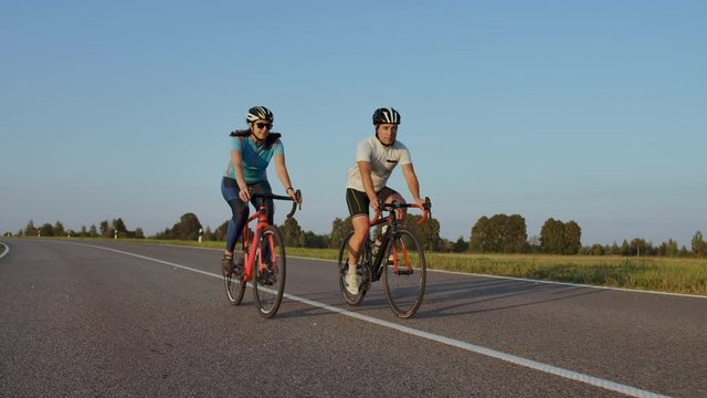 Front view of a young couple or friends riding their bikes in the city park or boulevard in summertime. People, leisure and lifestyle concept.