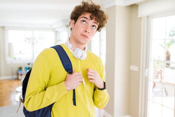 Young student man wearing headphones and backpack serious face thinking about question, very confused idea