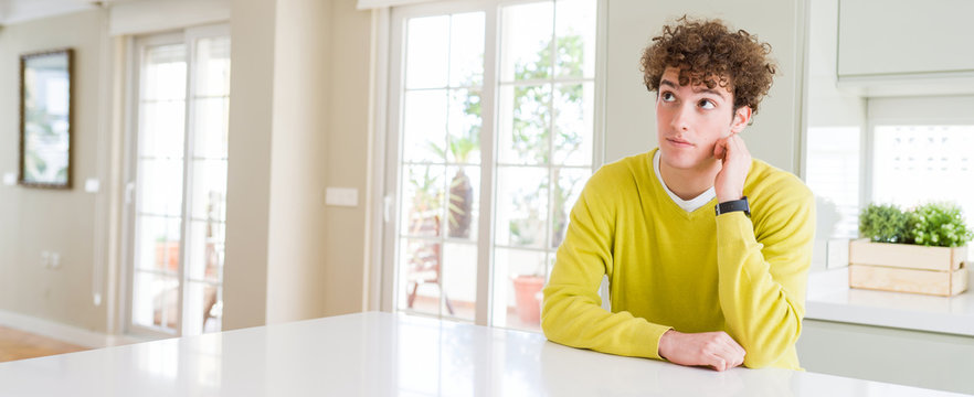 Wide angle shot of young handsome man at home thinking looking tired and bored with depression problems with crossed arms.