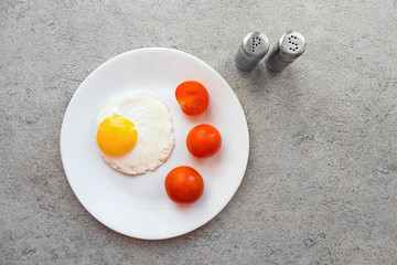 Fried eggs on a white plate with three tomatoes on a gray marble table. Salt and pepper shaker