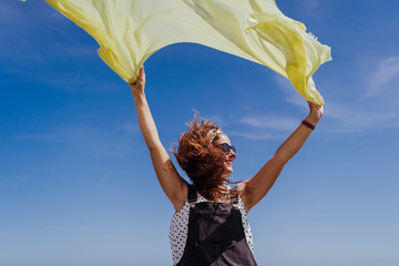 young caucasian woman outdoors playing with yellow scarf on a windy and sunny day. Lifestyle and...