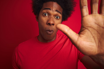 Young american man with afro hair wearing t-shirt standing over isolated red background with open...