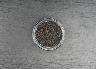 Sesame seeds in glass container on a black stone background.