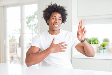 Young african american man wearing casual white t-shirt sitting at home smiling swearing with hand...
